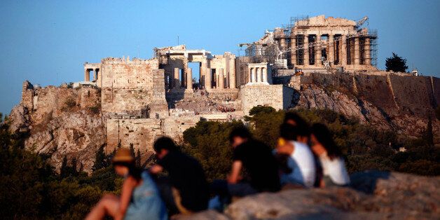 Tourists sit on rocks with a view of the Parthenon temple on Acropolis Hill in Athens, Greece, on Tuesday, Aug. 20, 2013. A third aid program for Greece announced by German Finance Minister Wolfgang Schaeuble yesterday will be partially financed through the EU budget. Photographer: Angelos Tzortzinis/Bloomberg via Getty Images