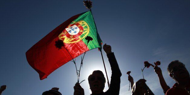 People holding red carnations and a Portuguese flag sing a protest song during a rally marking the international May Day, in Lisbon, Thursday, May 1, 2014. Beside defending labor rights, protesters shouted slogans against the austerity measures that the Portuguese government has been taking since the country was rescued by international creditors in 2011. (AP Photo/Francisco Seco)