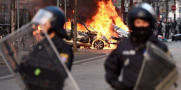 Riot Police form a cordon as a Police car burns on the opening day of the European Central Bank (ECB) in Frankfurt am Main, western Germany, on March 18, 2015. Supporters of the so-called Blockupy alliance consisting of social movements, activists, workers, trade unions and parties are expected to stage large protests against austerity and the authority of the European Central Bank when the bank's new headquarters officially will be on March 18, 2015. AFP PHOTO / ODD ANDERSEN (Photo