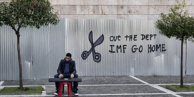 A man plays music on a digital keyboard near graffiti on a corrugated metal gate reading 'Cut the debt, IMF go home' in Athens on February 24, 2015. Greece edged closer to eurozone survival on February 24 as its international creditors and hold-out Germany looked ready to approve the reforms they had demanded of Athens in return for extending its bailout programme. AFP PHOTO / LOUISA GOULIAMAKI (Photo credit should read LOUISA GOULIAMAKI/AFP/Getty Images)
