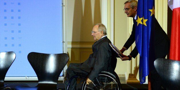 German Finance Minister Wolfgang Schaeuble (L) arrives on his wheelchair pushed by his spokesman Martin Jaeger for a press conference with his French counterpart on December 2, 2014 at the Finance ministry in Berlin following a meeting to discuss how to revive the struggling eurozone. AFP PHOTO / JOHN MACDOUGALL (Photo credit should read JOHN MACDOUGALL/AFP/Getty Images)