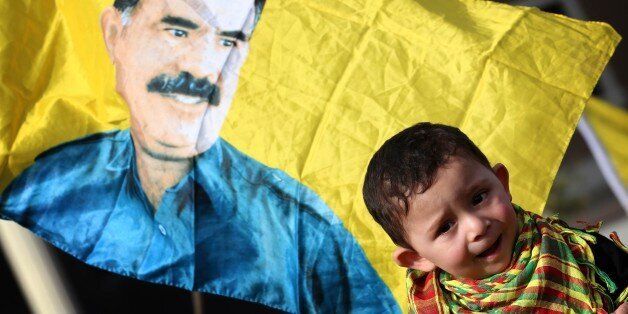 A child is seen in front of a flag bearing a portrait of the leader of the Kurdistan Workers Party (PKK) Abdullah Ocalan during a demonstration calling for his release on February 15, 2015 outside the Turkish consulate in Arbil, the capital of the autonomous Kurdish in Arbil. Ocalan was captured by Turkish undercover agents in Kenya in 1999, brought back to Turkey and sentenced to death. His sentence was later commuted to life. AFP PHOTO / SAFIN HAMED (Photo credit should read SAFIN HAME