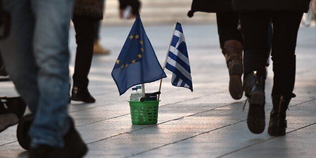 People walk next to a Greek and an EU flag in Athens on February 25, 2015. The hard work for Greece's new anti-austerity government began Wednesday of living up to promises made not only to international creditors but also to voters expecting relief from years of painful cuts. AFP PHOTO / ARIS MESSINIS (Photo credit should read ARIS MESSINIS/AFP/Getty Images)