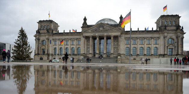 The German parliament building 'Reichstag' is mirrored in a puddle as tourists take pictures, in Berlin, Tuesday Dec. 23, 2014. (AP Photo/dpa, Rainer Jensen)