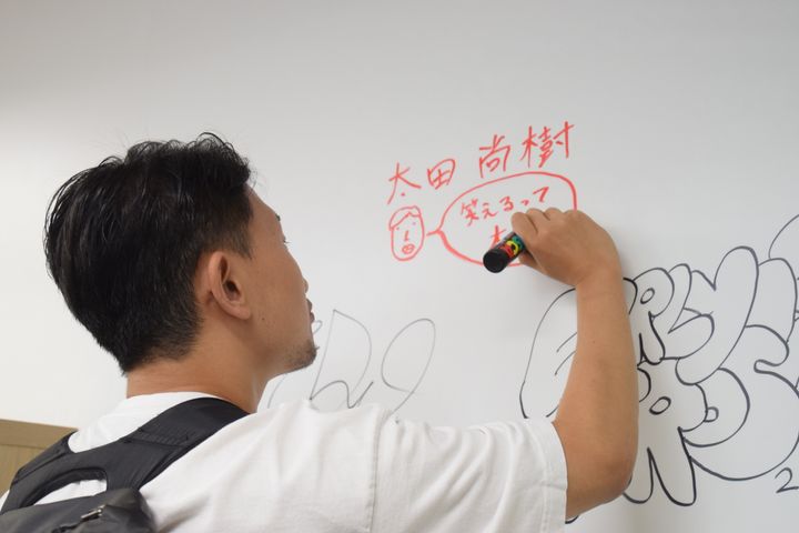太田尚樹さん。ハフポスト日本版のオフィスの壁に「笑えるって大事」とメッセージを書いてくれた