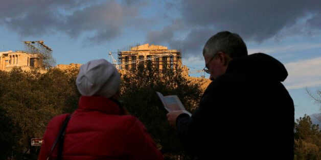 Tourists read a map while looking towards the Parthenon temple on Acropolis Hill in Athens, Greece, on Thursday, Jan. 8, 2015. Greek Prime Minister Antonis Samaras's effort to overhaul opposition Syriza party's lead before elections in less than three weeks is running out of steam, polls show. Photographer: Kostas Tsironis/Bloomberg via Getty Images