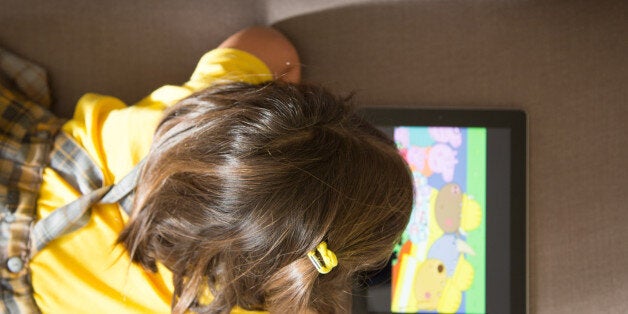 Girl watching cartoons online with the iPad tablet laying in the sofa at home with view from above.