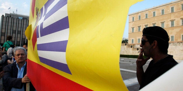 A riot police smokes a cigarette as an elderly man holds a banner with Spanish and Greek flags in front of the Greek Parliament during a peaceful rally for a sixth day, attended by thousands called through a social networking site - modeled on protests by young people in Spain, on Monday, May 30, 2011. Greece could get another euro 20 billion ($28 billion) in aid from its fellow euro countries and raise three times that through new austerity measures such as selling government property, a top Eu