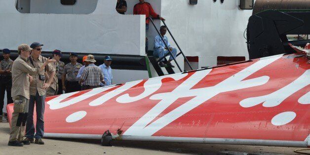 Foreign investigators (L) examine the tail of the AirAsia flight QZ8501 in Kumai on January 12, 2015, after debris from the crash was retrieved from the Java sea. Indonesian divers retrieved the flight data recorder of the AirAsia plane that went down in the Java Sea a fortnight ago with 162 people on board, a crucial breakthrough that should help explain what caused the crash. AFP PHOTO (Photo credit should read STR/AFP/Getty Images)