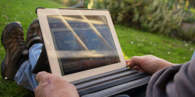 A man watches basketball on his iPad while sitting outside in his garden in the evening.