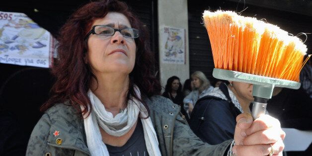 ATHENS, GREECE - 2014/05/07: A cleaning lady, a former employee in the ministry of Finance in Greece holds a mop symbol of her work and a sign of protest. Hundreds of people took part in a protest, demanding that the Greek government revokes its decision to lay off public sector workers under the financially troubled country's bailout commitments. (Photo by George Panagakis/Pacific Press/LightRocket via Getty Images)