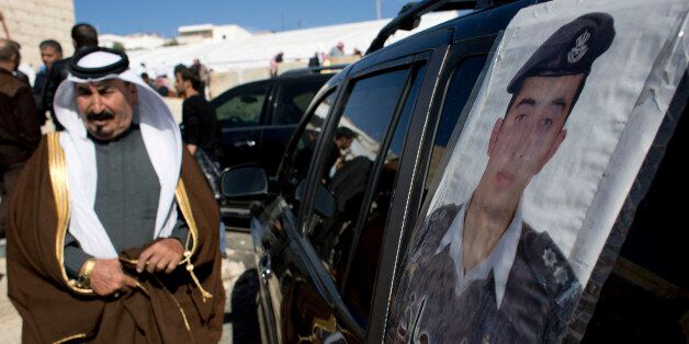 A Jordanian man walks past a poster that is pasted on a vehicle with a picture of slain Jordanian pilot, Lt. Muath al-Kaseasbeh with Arabic that reads,