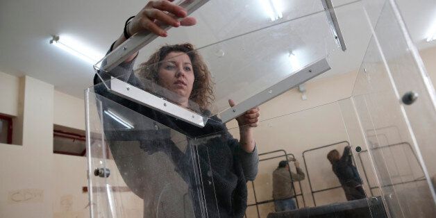 The head of a polling station Evangelia Darara places the lid on a ballot box as municipal workers assemble voting booths, Athens, Friday, Jan. 23, 2015. Prime Minister Antonis Samaras' New Democracy party has failed so far to overcome a gap in opinion polls with the anti-bailout Syriza party ahead of the Jan. 25 general election. (AP Photo/Petros Giannakouris)