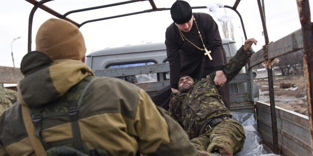 Pro-Russian rebels help a priest to put bodies of killed Ukrainian soldiers in a truck on a check point captured by pro-Russian rebels at the town of Krasniy Partizan, eastern Ukraine, Saturday, Jan. 24, 2015. The fighting continues despite several cease fire declarations. (AP Photo/Mstyslav Chernov)