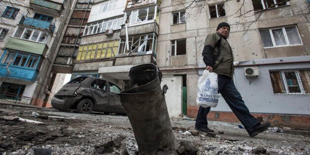 A man walks by a burned car and a piece of exploded Grad missile, outside an apartment building in Vostochniy district of Mariupol, Eastern Ukraine, Sunday, Jan. 25, 2015. Indiscriminate rocket fire slammed into a market, schools, homes and shops Saturday in Ukraine's southeastern city of Mariupol, killing at least 30 people, authorities said. The Ukrainian president called the blitz a terrorist attack and NATO and the U.S. demanded that Russia stop supporting the rebels. (AP Photo/Evgeniy Maloletka)