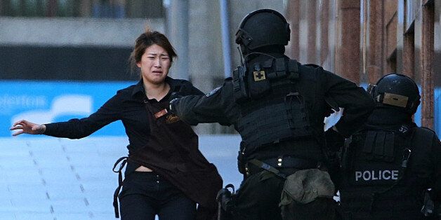 A hostage runs to armed tactical response police officers for safety after she escaped from a cafe under siege at Martin Place in the central business district of Sydney, Australia, Monday, Dec. 15, 2014. The siege ended just after 2 a.m. in a barrage of gunfire when police rushed in to free the remaining captives. Two hostages, including Tori Johnson, the cafe manager, were killed. So was the gunman. (AP Photo/Rob Griffith)
