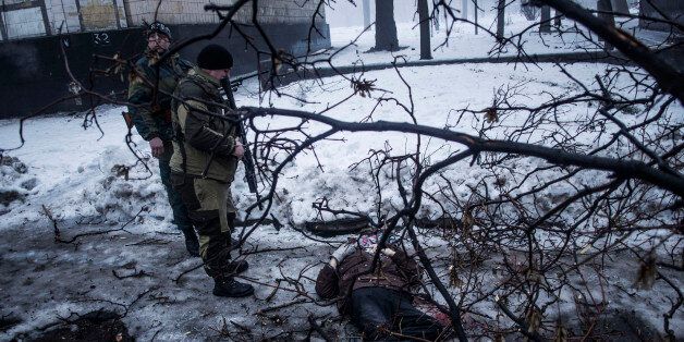 Separatist rebels look at the body of a man killed near a bus stop that was hit by Ukrainian army shells in Donetsk, eastern Ukraine, Tuesday, Jan. 20, 2015. At least three civilians were killed in shelling Tuesday in eastern Ukraine as fighting continued between government and rebel forces in the separatist-held city of Donetsk. (AP Photo/Manu Brabo)