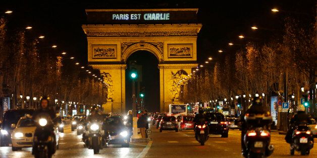 Motorcyclists ride on the Champs Elysees with the Arc de Triomphe displaying the solidarity message
