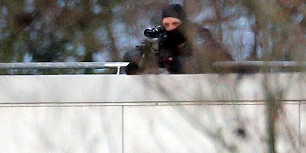 A hooded police officer aim from a rooftop in Dammartin-en-Goele, northeast of Paris, where the two brothers suspected in a deadly terror attack were cornered, Friday, Jan.9, 2015. Two sets of attackers seized hostages and locked down hundreds of French security forces around the capital on Friday, sending the city into fear and turmoil for a third day in a series of linked attacks that began with the deadly newspaper terror attack that left 12 people dead. (AP Photo/Christophe Ena)
