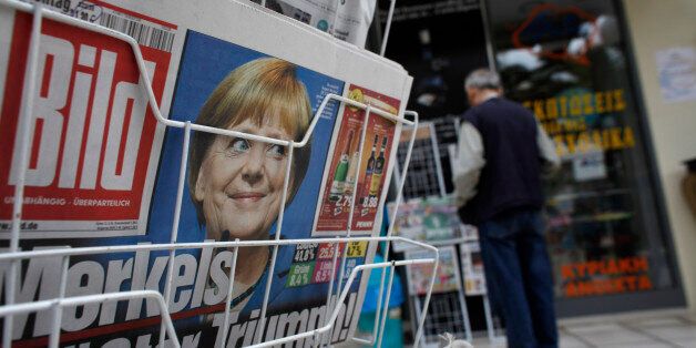A photograph of Germany's Chancellor Angela Merkel looks out from the front page of Bild on a newspaper stand following her election victory, in Corinth, Greece, on Monday, Sept. 23, 2013. While the country's lenders are on firmer footing after getting capital from euro-area and International Monetary Fund bailout funds, they still need to reduce the non-performing loans that have tripled to 29 percent of the total in three years and threaten their new-found solvency. Photographer: Kostas Tsiron