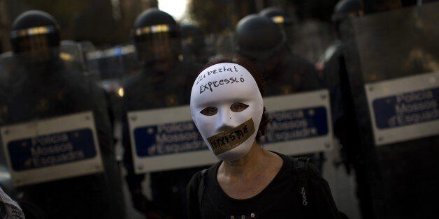 A woman wearing a mask stands in front of riot police officers cordon off the area during a protest against Spanish Citizens Security Law in Barcelona, Spain, Saturday, Dec. 20, 2014. Thousands of people have gathered in several Spanish cities to protest against a new law that sets hefty fines for offenses such as burning the national flag and holding demonstrations outside parliament buildings or strategic installations. The writing on the woman's mask reads in Catalan