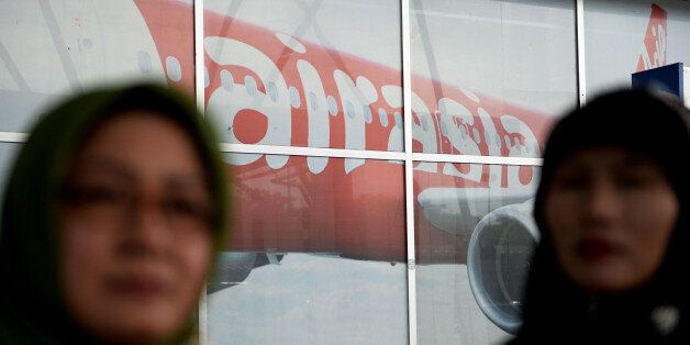 Travelers stand in front of an advertisement for AirAsia Bhd. in a departure hall at Soekarno-Hatta International Airport in Cengkareng, near Jakarta, Indonesia, on Monday, Dec. 29, 2014. Planes and ships from four nations scoured the Java Sea for an AirAsia passenger jet that vanished off the coast of Borneo more than a day ago with 162 people on board, as Indonesian investigators said the jet had likely crashed to the bottom of the sea. Photographer: Dimas Ardian/Bloomberg via Getty Images