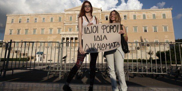 A lesbian couple Christina, left, and Ioanna hold a banner that reads ''Same taxes, same rights'' during a protest outside Greece's Parliament in Athens on Friday, Sept. 5, 2014. Several hundred people took part in the peaceful march to Parliament, which is debating draft legislation to outlaw Holocaust denial and expand prosecution powers against the incitement of racial violence. Gay and Lesbian rights groups complain that the proposed legislation will not adequately address attacks on homosexual people, which they say are on the rise. (AP Photo/Thanassis Stavrakis)