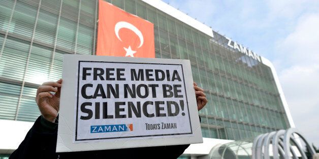 A man holds a placard as people gather in support outside Zaman newspaper in Istanbul, Turkey, Sunday, Dec. 14, 2014, hours after police launched raids in a dozen cities, detaining at least 23 people, including journalists, television producers and police known to be close to a movement led by a U.S.-based moderate Islamic cleric Fethullah Gulen. The government accuses the Gulen's movement, a former ally, of orchestrating an alleged plot to try and bring down the government. It says the group's