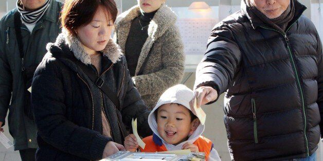 A boy (C) helps his mother (L) to cast a vote in Japan's general election at a polling station in Tokyo on December 14, 2014. Japanese voters went to the polls for a general election likely to return Prime Minister Shinzo Abe to power, and billed as a referendum on his economic policy. Polling stations opened early across the nation in a lower house election with 1,191 candidates vying for 475 seats. AFP PHOTO / Yoshikazu TSUNO (Photo credit should read YOSHIKAZU TSUNO/AFP/Getty Images)