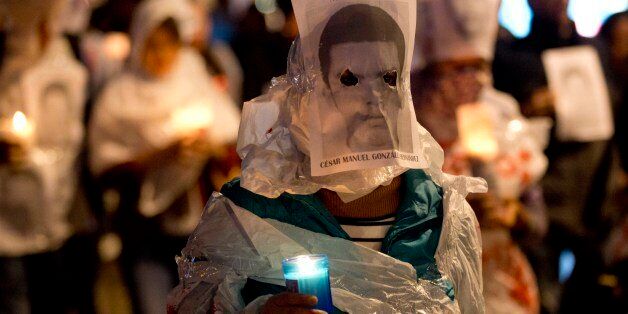 A demonstrator holds a candle, wearing an image of one of the 43 students who were disappeared, in Mexico City, Friday, Nov. 14, 2014. The 43 teachers-school students disappeared at the hands of a city police force on Sept. 26 in the town of Iguala. (AP Photo/Eduardo Verdugo)