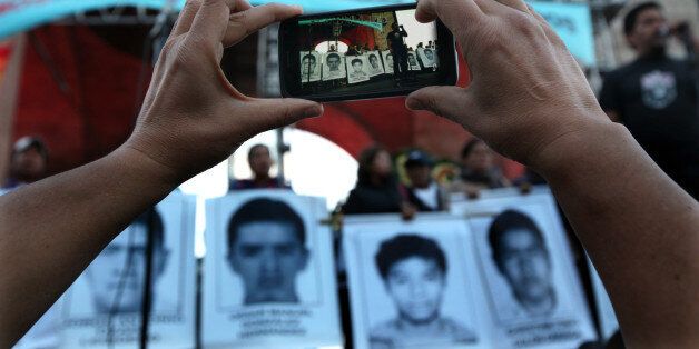 A protester takes a photo of the relatives of 43 missing students from the Isidro Burgos rural teachers college standing on a stage during a protest in Mexico City, Saturday, Dec. 6, 2014. At least one of the college students missing since September has been identified among charred remains found near a garbage dump, two Mexican officials confirmed Saturday. A family member of a missing student told The Associated Press that the remains were of Alexander Mora. The students went missing Sept. 26