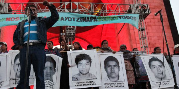 Felipe de la Cruz, the father of one of the 43 missing students from the Isidro Burgos rural teachers college, speaks to a crowd in front of other relatives holding posters of their missing loved ones, during a protest at the Revolution Monument in Mexico City, Saturday, Dec. 6, 2014. At least one of the college students missing since September has been identified among charred remains found near a garbage dump, two Mexican officials confirmed Saturday. A family member of a missing student told