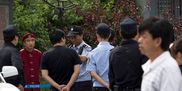 A security guard, second from left in red uniform, watches a policeman try out a device used to restrain...
