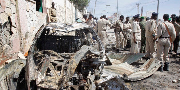 Somali soldiers stand by wreckage at the scene of a suicide car bomb attack that targeted a United Nations convoy, outside the airport in Mogadishu, Somalia Wednesday, Dec. 3, 2014. A Somali police officer says a suicide bomber rammed his vehicle into a U.N. convoy near Mogadishu's airport, killing three people. (AP Photo/Farah Abdi Warsameh)