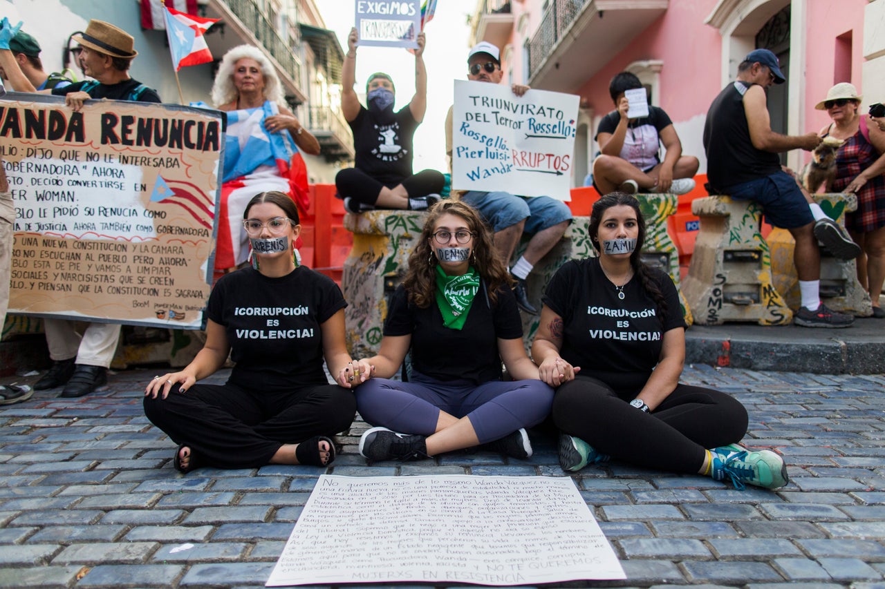 Tres mujeres protestan con otros manifestantes afuera de La Fortaleza, la mansión del gobernador, en San Juan el 9 de agosto, 2019.