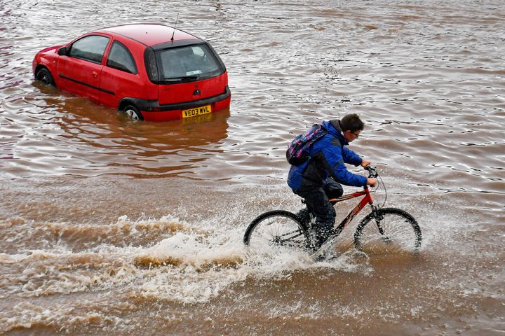 A man cycles past a stranded car on a flooded road in Birmingham city centre. The Met Office has issued a yellow weather warning for much of England and Wales today, with flooding expected in some areas.