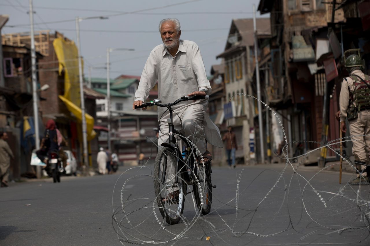 A Kashmiri cyclist rides past barbwire set up as road blockade in Srinagar on Sept. 20.