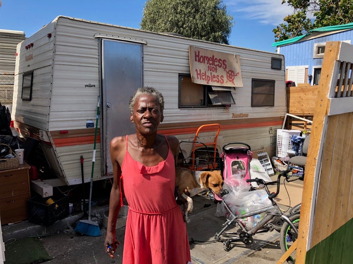 Claudette Smith stands in front of her mobile home in an Oakland homeless encampment, with a sign that reads: "Homeless not h