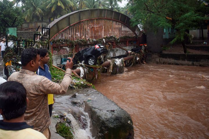 Onlookers and residents take photos of a car washed away by flash floods following heavy overnight rains in Pune on September 26, 2019. 
