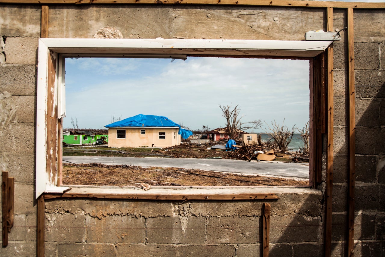 Through a broken window, homes are seen being covered up by their residents and trash being thrown to the front of the house to help clear the inside of the structures in East End, Grand Bahama.