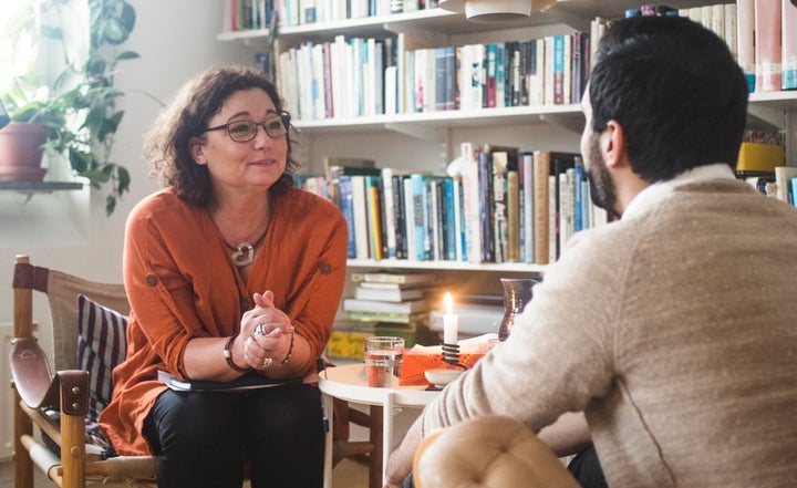 Female therapist listening to young patient by bookshelf at home office