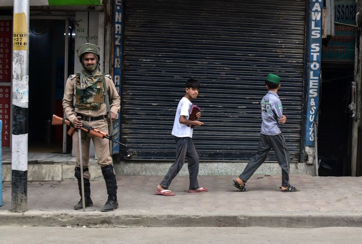 Children walk past a paramilitary trooper during restrictions in Srinagar, Kashmir. 