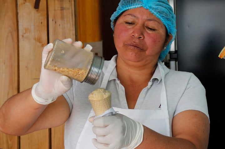 In this Sept. 28, 2019 photo, Maria del Carmen Pilapana tops a scoop of a guinea pig flavored ice cream with peanuts, at her stall on the outskirts of Quito, Ecuador. Out of work, with three children in tow, Pilapana began attending free training courses for entrepreneurs. She was challenged to do something innovative and, after six months of testing, she starting selling offbeat flavored ice creams. (AP Photo/Dolores Ochoa)