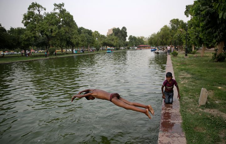 An Indian boy jumps into a pond near the India Gate monument on a hot day in New Delhi, India.