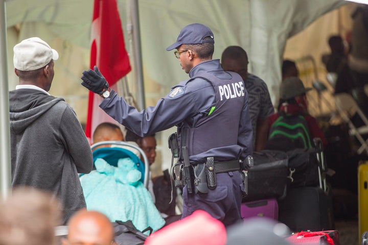 A Royal Canadian Mounted Police officer talks to migrants after they crossed the Canada/U.S. border near Hemmingford, Que. on August 6, 2017.