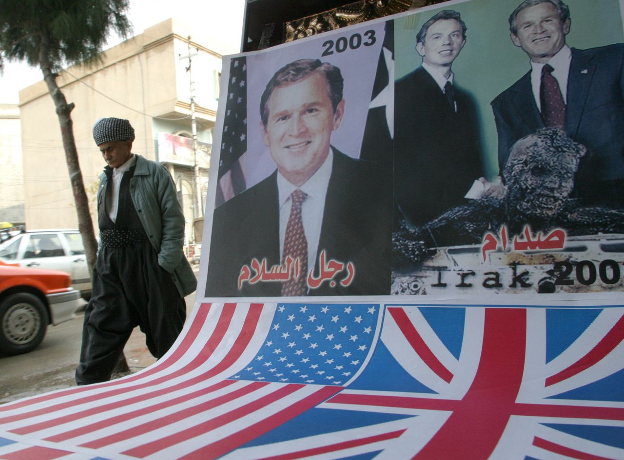 Ένας Κούρδος του Ιράκ, σε δρόμο της Σουλαϊμανίγια, έξω από τη Βαγδάτη περνά δίπλα από μια αφίσα των Μπους και Μπλε (Δεκέμβριος 2003). 