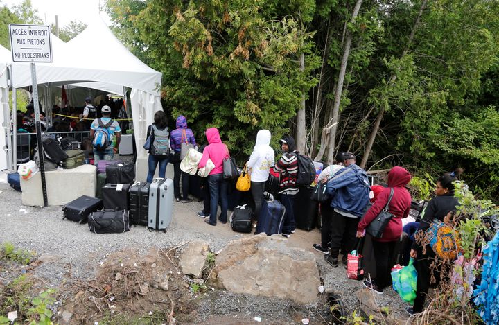 A line of asylum seekers who identified themselves as from Haiti wait to enter into Canada from Roxham Road in Champlain, N.Y. on Aug. 7, 2017. 