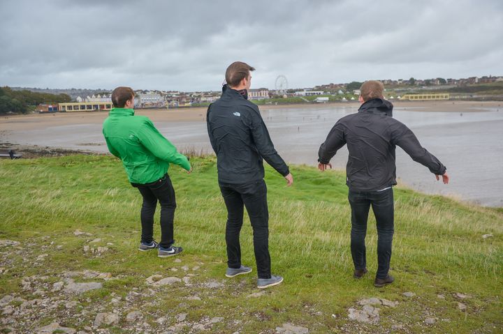Three men lean into the wind on the headland at Barry Island.