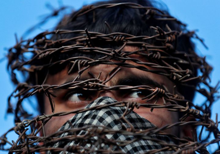A masked Kashmiri man with his head covered with barbed wire attends a protest after Friday prayers during restrictions in Srinagar, October 11, 2019. 