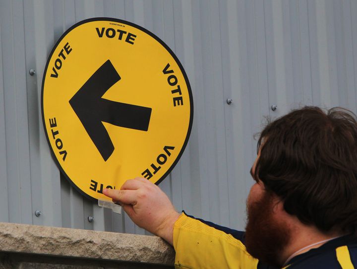 Elections Canada information officer Steven Moyer tapes a voting direction arrow sign to the fire hall in Kerwood, Ont., on Oct. 19, 2015.